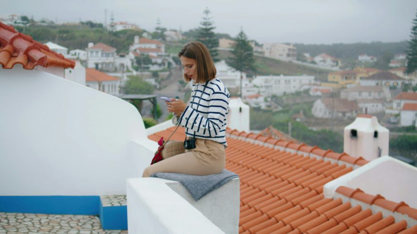 Tourist checking social media at mediterranean cityscape. Smiling travel blogger