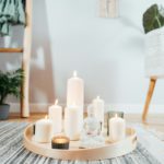 Wooden tray with burning candles and white Buddha statuette on the floor of modern interior.
