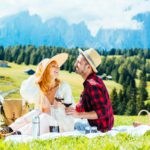 Young couple drinking red wine sitting on countryside field