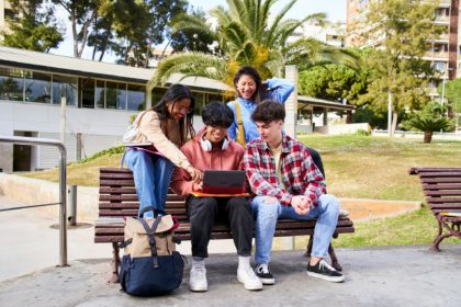 Young international college students reading books, studying on laptop, preparing for exam