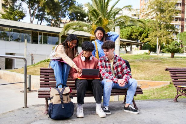 Young international college students reading books, studying on laptop, preparing for exam